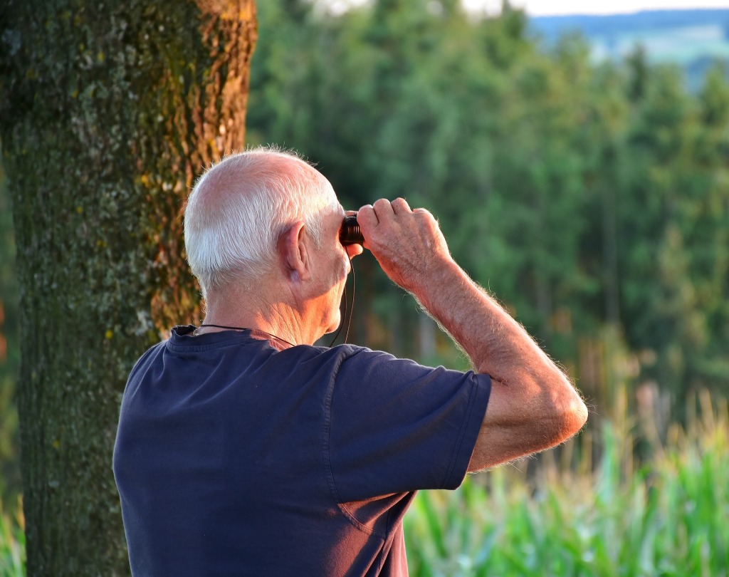 An elderly man looking into the distance with binoculars.
