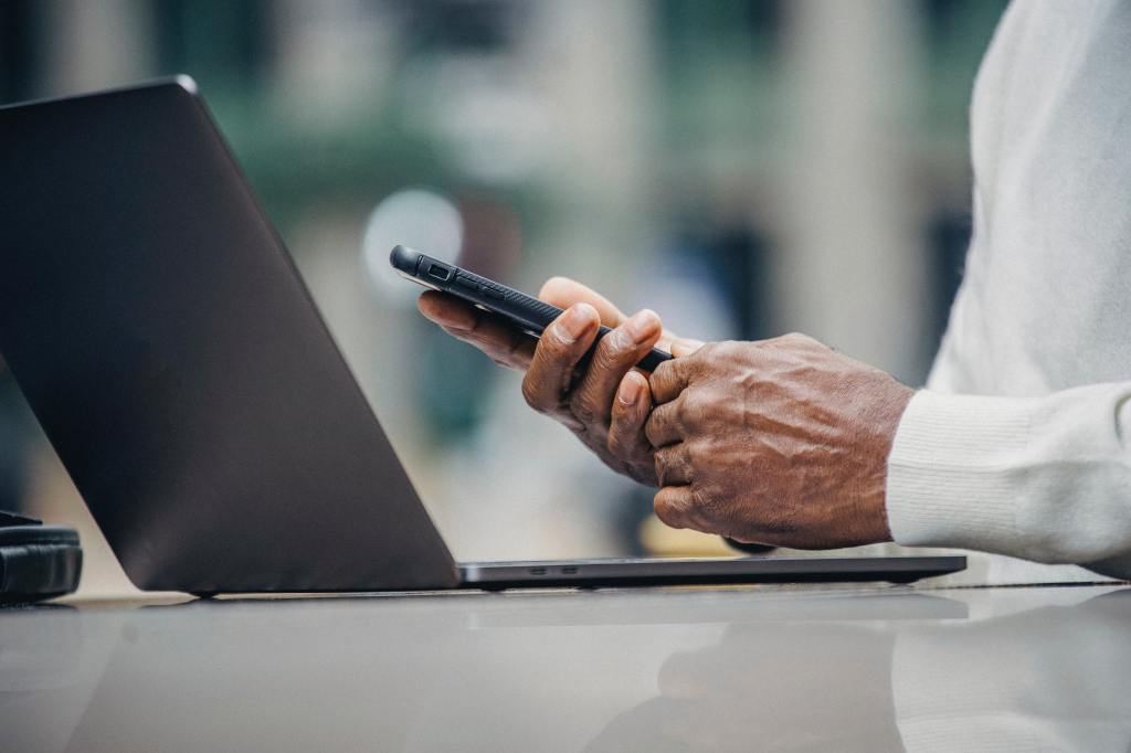 An elderly man using a smart phone and a laptop.