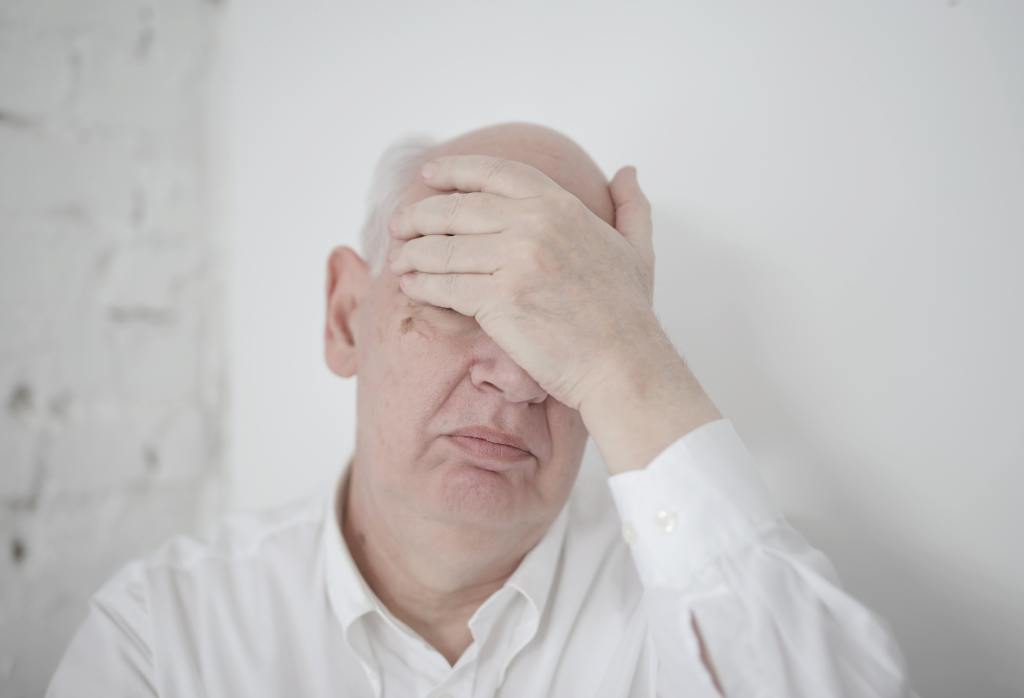 An elderly man covering his face with his hand.