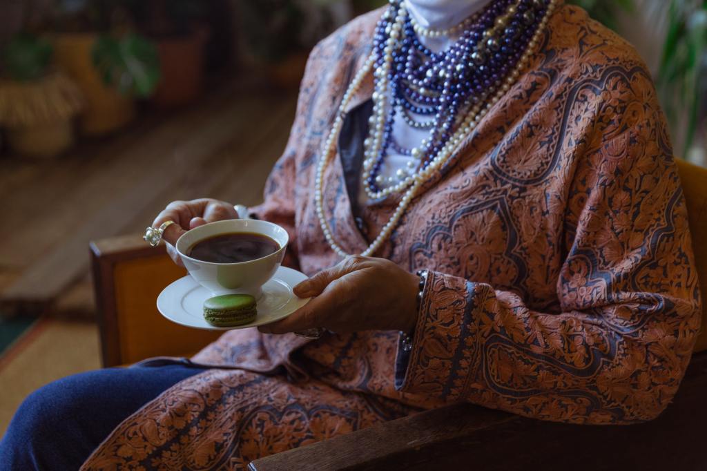 An elderly woman drinking tea while sitting down.