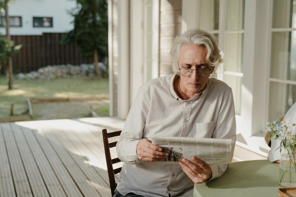 An elder reading a newspaper outside.