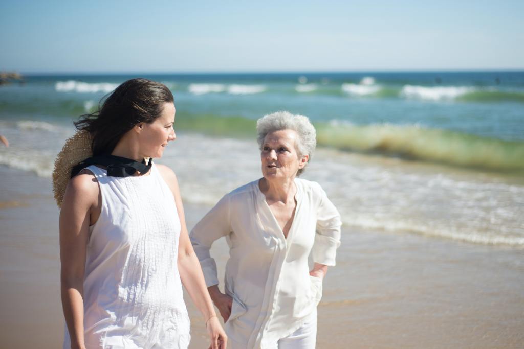 A woman walking on a beach with an elderly woman.
