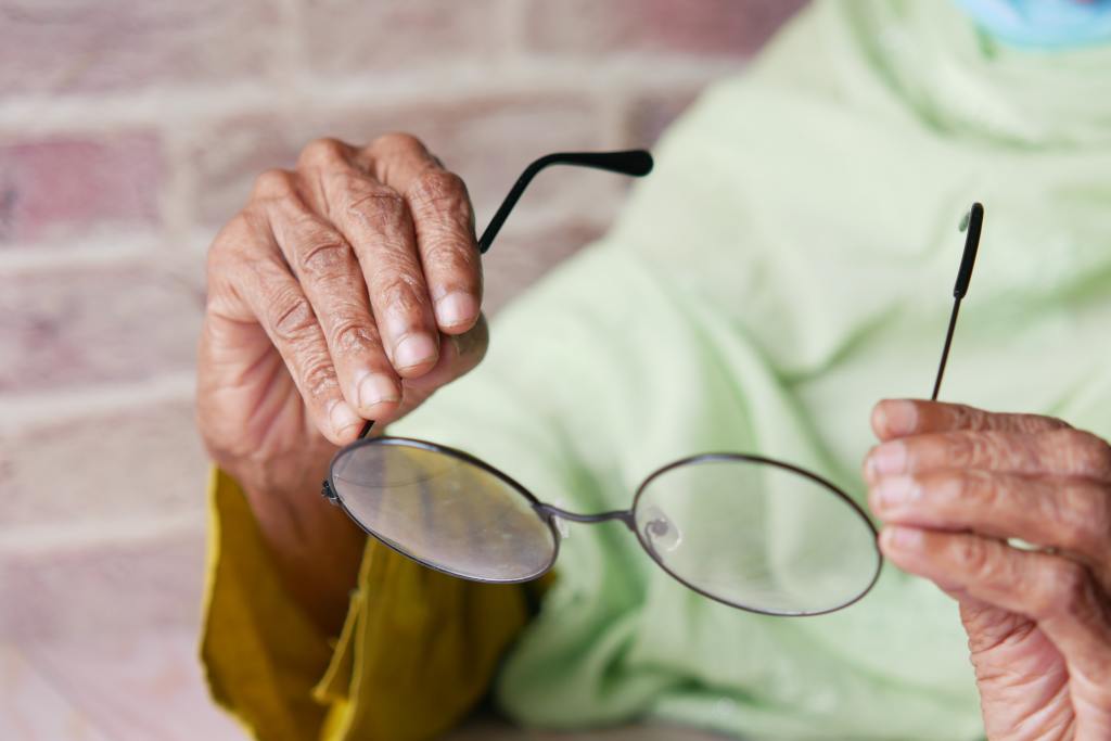 A elderly person holding up glasses.