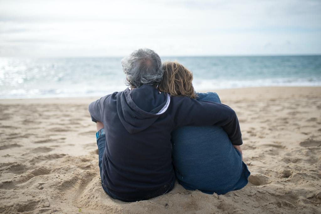 An older couple sitting on the beach sand.